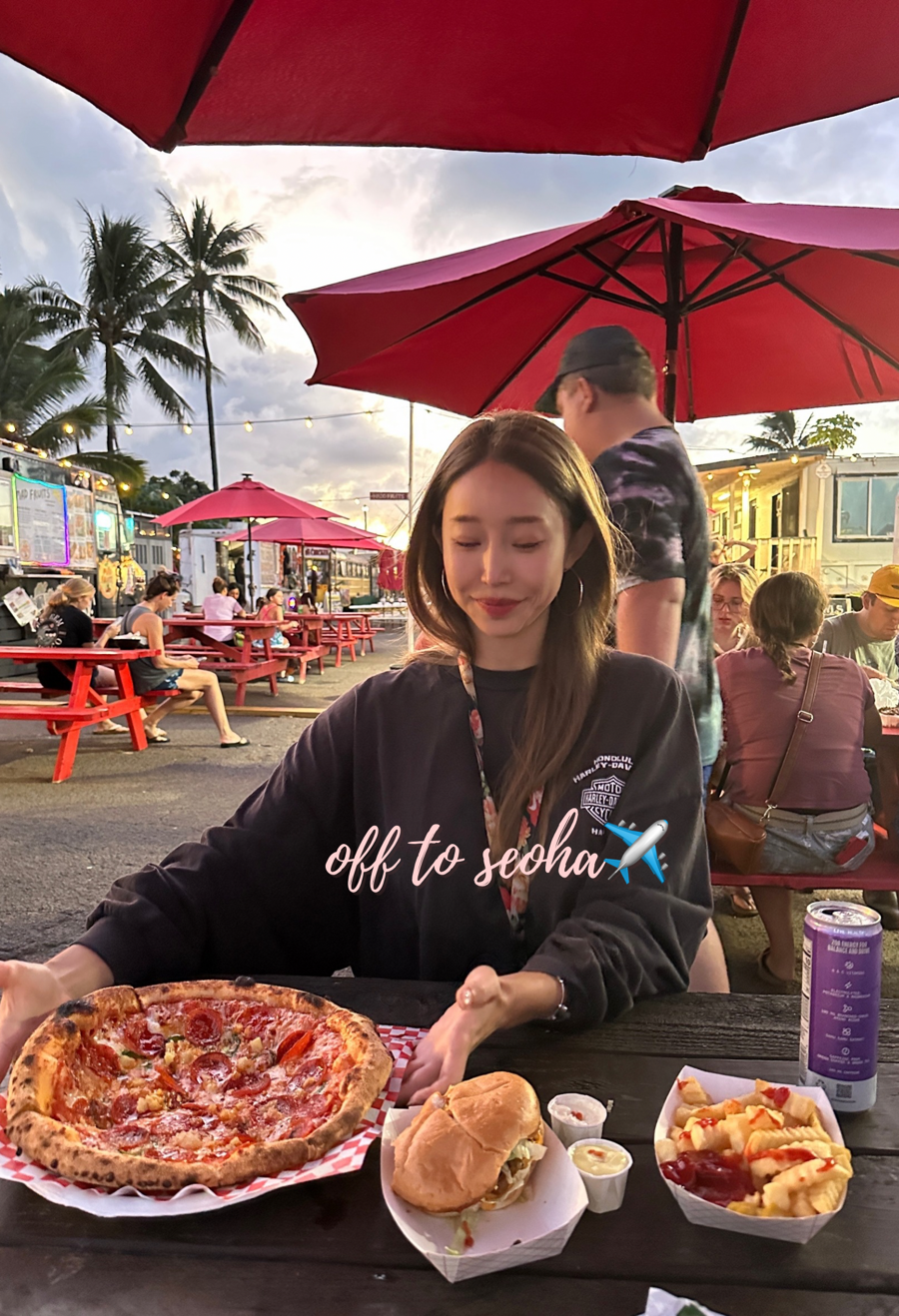Outdoor seating under red umbrellas at Kahuku food truck zone during sunset in Hawaii