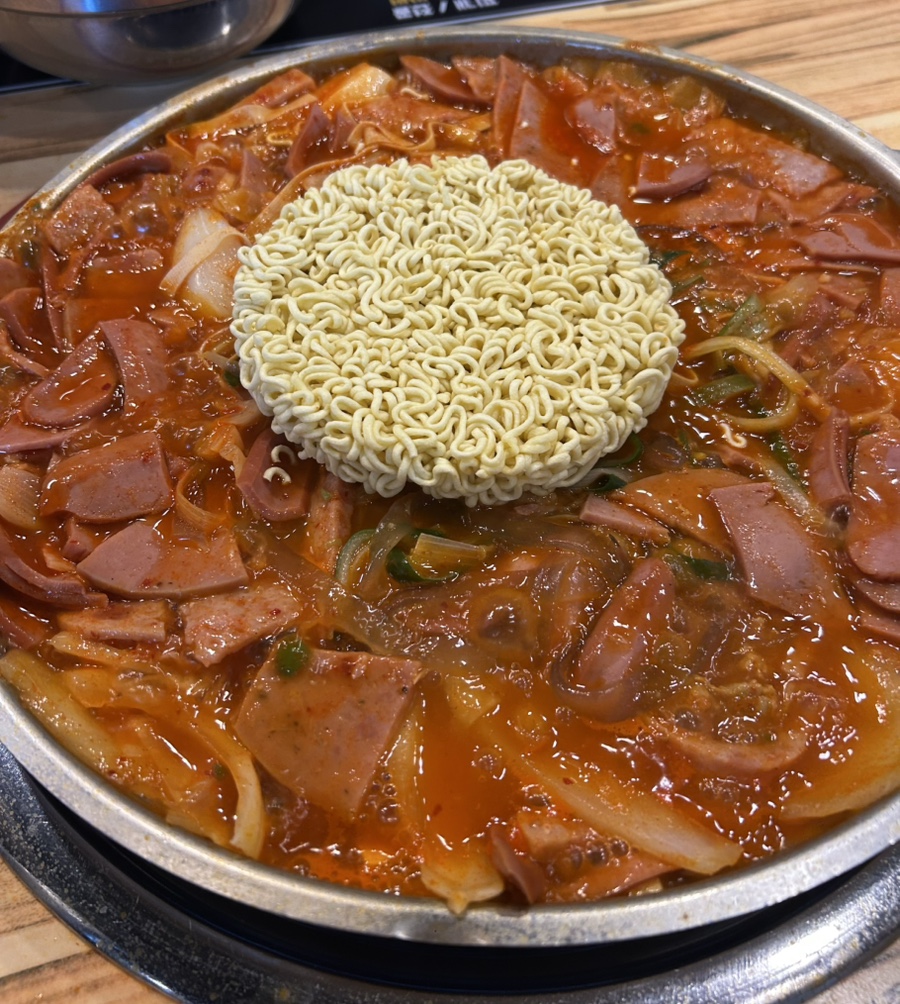 붉은 부대전골 육수와 햄 위에 동그란 라면사리가 올려진 냄비