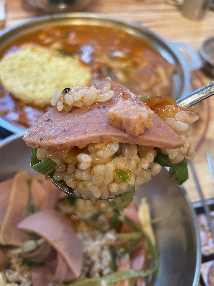 숟가락 위에 국물에 적신 밥과 큼직한 햄이 올려진 모습