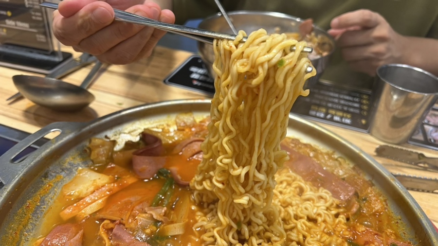 부대전골 냄비에서 끓여진 라면사리를 젓가락으로 집어 올리는 모습