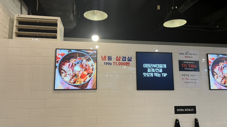 타일 벽면에 걸린 메뉴 사진 액자와 부대찌개 맛있게 먹는 팁 안내판